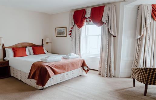 A cosy hotel room with a comfortable bed, a chair, and a window offering a scenic view.
