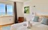 Mangersta Steading Bedroom, king size double bed, white bed linen and towels, patterned cushions. A sea view window, leather chair, oil painting.