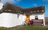 Ticket To Ride white thatched cottage with bike outside