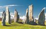 The ancient Callanish Stones on the Isle of Lewis, towering upright in a mystical landscape under a blue sky.